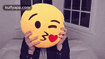 a person is covering their face with an emoji pillow .
