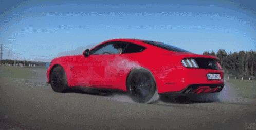 a red ford mustang is driving down a road with smoke coming out of it
