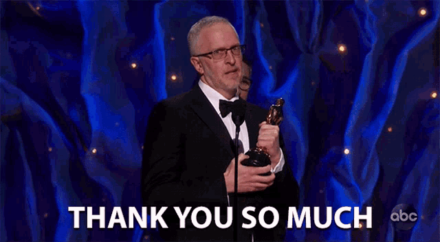 a man in a tuxedo holding a trophy with the words thank you so much behind him