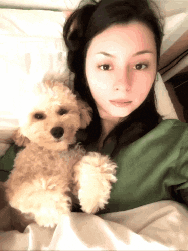 a woman laying in bed with a small brown dog