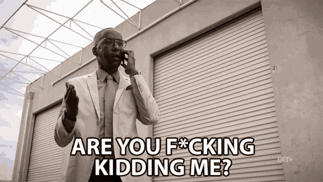 a man in a suit talking on a cell phone with the words are you f * cking kidding me