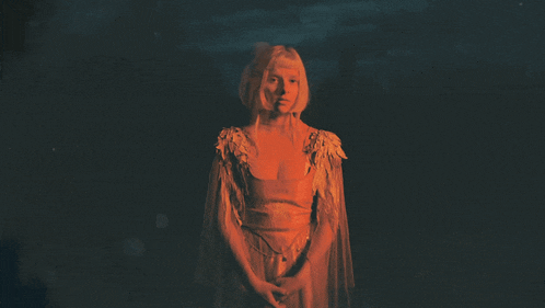 a woman in a dress with wings on the sleeves is standing in a dark room