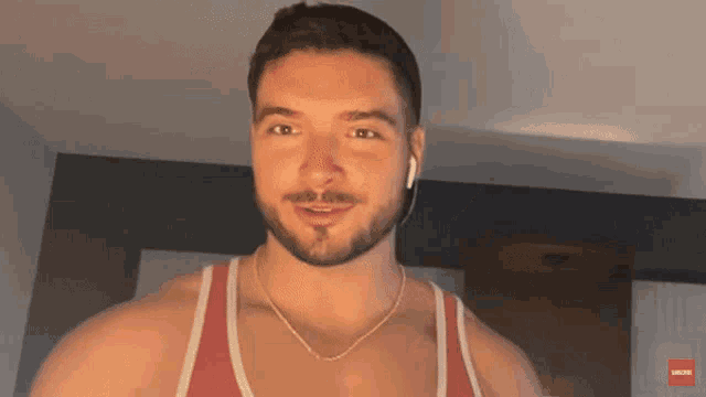 a man with a beard wearing a red tank top and a gold chain
