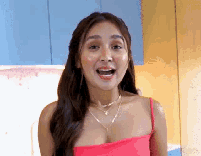 a woman in a pink top and necklace is standing in front of a blue cabinet .