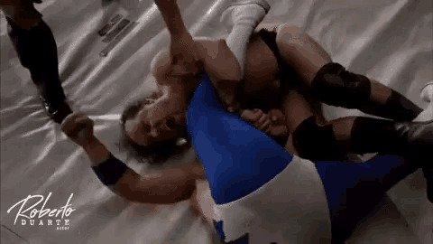 a man in a blue and white outfit is wrestling another man in a black and white outfit