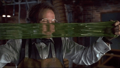 a man in a tuxedo and bow tie is holding a green substance over his face