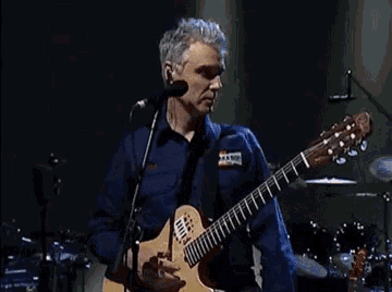 a man in a blue shirt is playing a guitar and singing into a microphone .