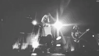 a black and white photo of a woman singing into a microphone while a man plays a guitar on stage .