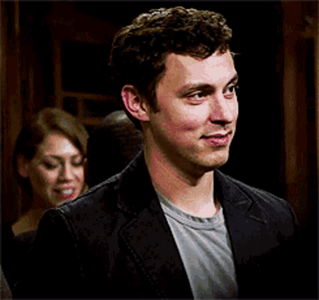 a man in a black jacket is smiling with a woman behind him