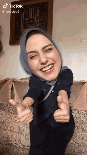 a woman wearing a blue hijab is giving a thumbs up