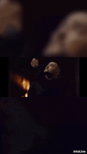 a man with a beard is standing in front of a fire with intolive written on the bottom
