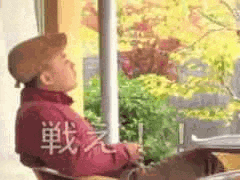 a man in a red jacket is sitting in front of a window .