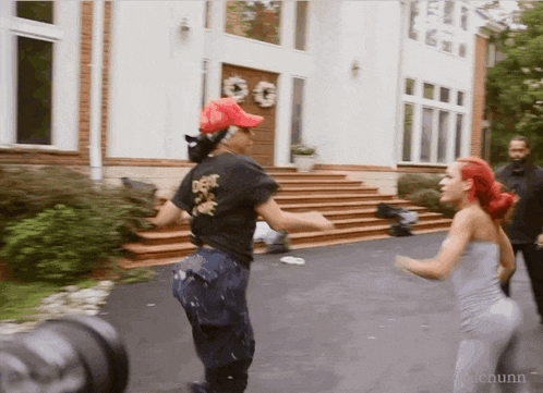 two women are dancing in front of a large white house and one of them is wearing a shirt that says do n't care