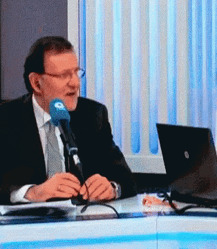 a man in a suit is sitting at a desk with a laptop and a microphone