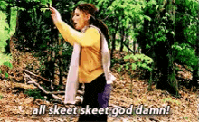 a woman in a yellow sweater is standing in the woods and says all skeet skeet god damn .