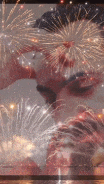 a man and woman are kissing in front of a fireworks display .