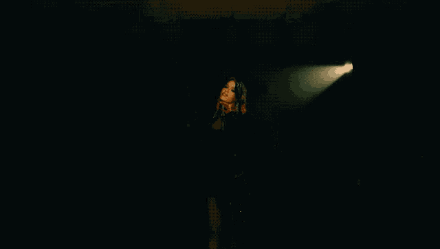 a woman with red hair is singing into a microphone in a dark room