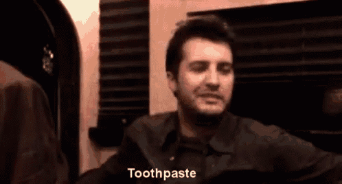 a man is smiling and pointing at the camera while saying toothpaste .