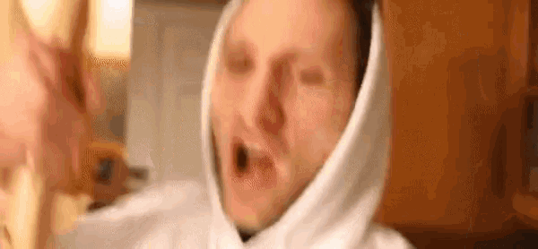 a man wearing a white hoodie is making a funny face with his mouth open .