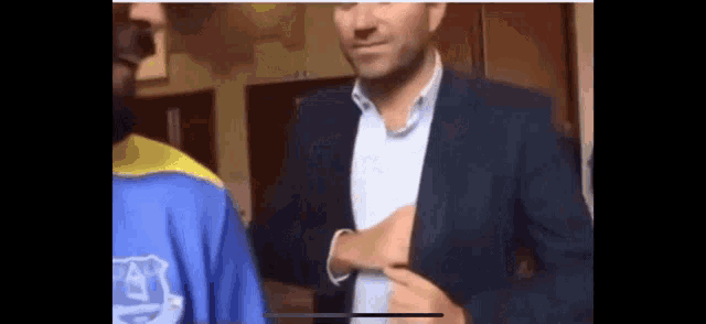 a man in a suit is standing next to a man in a blue shirt .