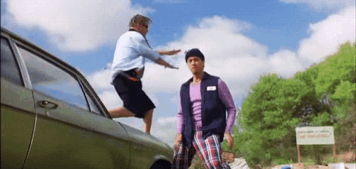 a man is jumping out of a car while another man stands next to him .
