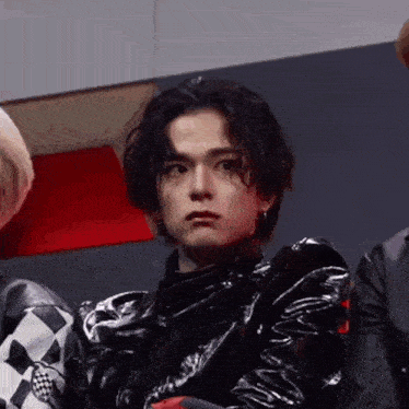 a young man wearing a black leather jacket and earrings is sitting in front of a group of people .