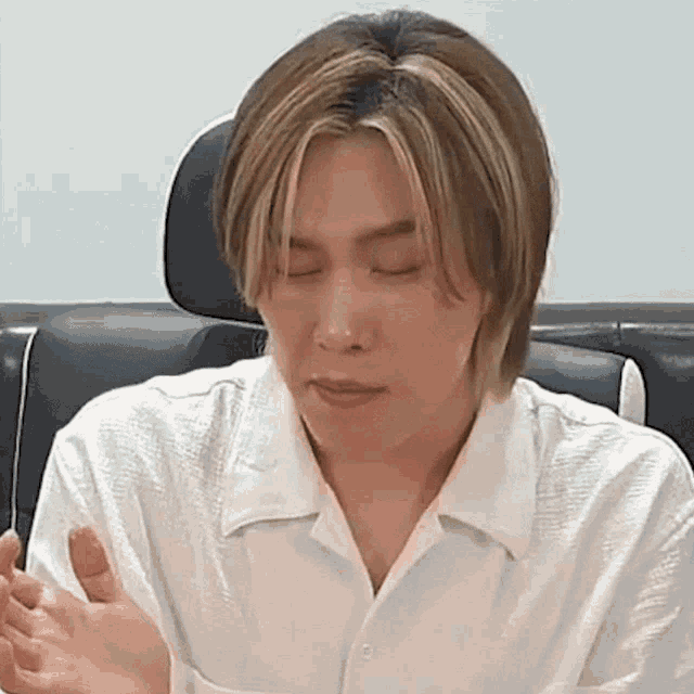 a man in a white shirt is sitting in a chair with his eyes closed and a bandage on his finger .