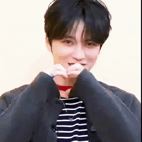 a young man is making a heart shape with his hands while wearing a striped shirt .
