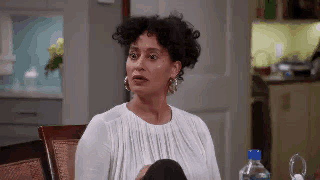 a woman is sitting at a table with a bottle of water and making a funny face .