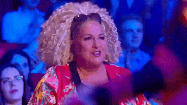 a woman with curly blonde hair is sitting in a crowd of people .