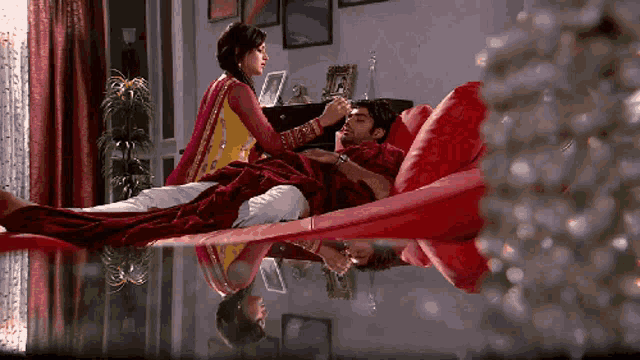 a man is laying on a red couch with a woman standing behind him