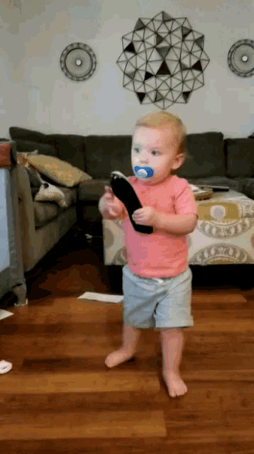 a baby with a pacifier in his mouth is holding a remote control in a living room