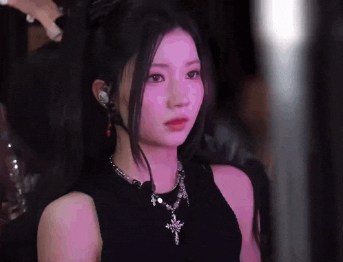a woman wearing a black top and a necklace with a cross on it is looking at the camera .