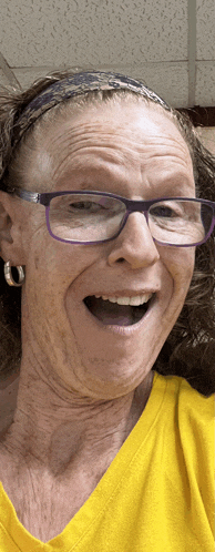 an elderly woman wearing glasses and a yellow shirt is smiling