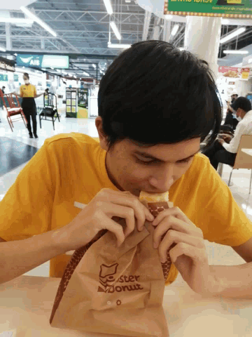 a man in a yellow shirt is eating a pastry from a mister donut bag