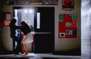 a man and a woman are fighting in a hallway in front of a sign that says ' athletics ' on it