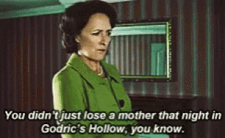 a woman in a green coat is standing in a room and talking to a man .