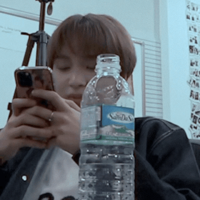 a person looking at their phone next to a bottle of soda
