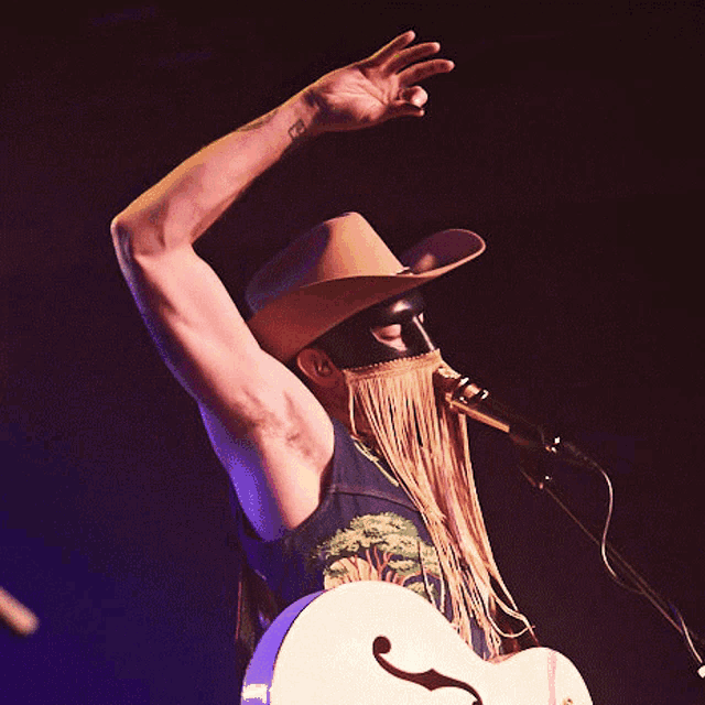 a man wearing a cowboy hat is singing into a microphone while playing a guitar