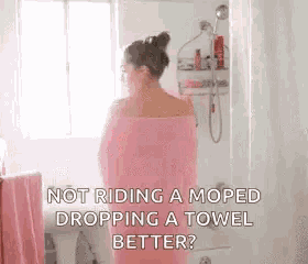 a woman wrapped in a pink towel is standing in a bathroom next to a window .