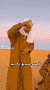 a man wearing a turban is standing in the desert with arabic writing on his face