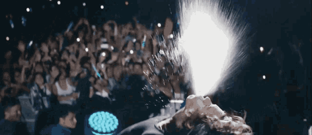a man is laying on a stage with a crowd behind him and spraying water into his face