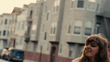 a woman is standing in front of a row of buildings and smiling