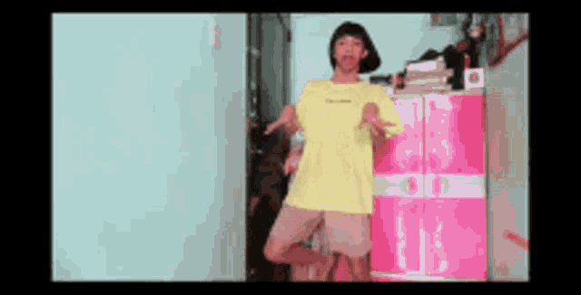 a girl in a yellow shirt is standing in front of a pink dresser