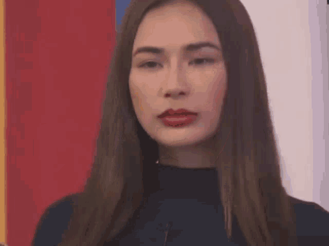 a woman with long brown hair and red lipstick is standing in front of a colorful wall .