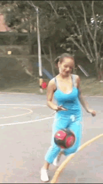 a woman in a blue tank top is kicking a soccer ball on a basketball court .