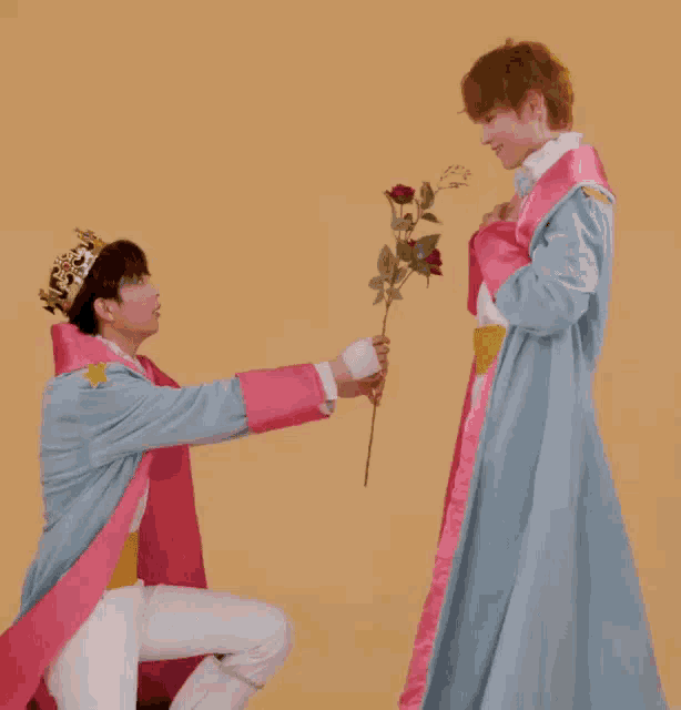 a man wearing a crown is kneeling down next to another man in a pink robe