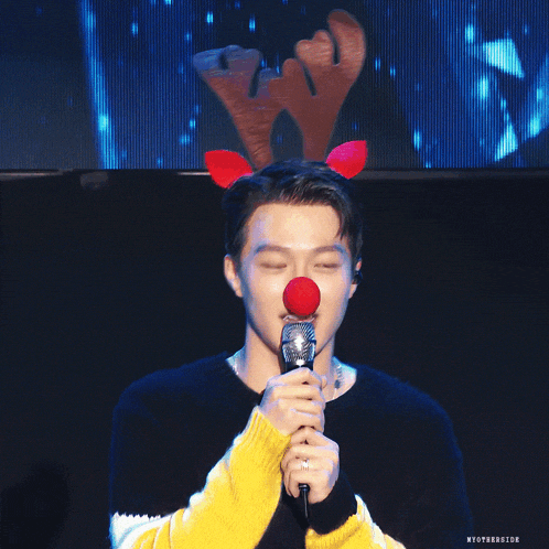 a man wearing a reindeer headband holds a microphone in his hand