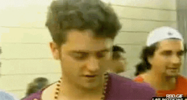 a man in a purple shirt with a necklace around his neck is standing in a crowd .
