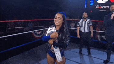 a woman in a wrestling ring holding a trophy with a referee in the background